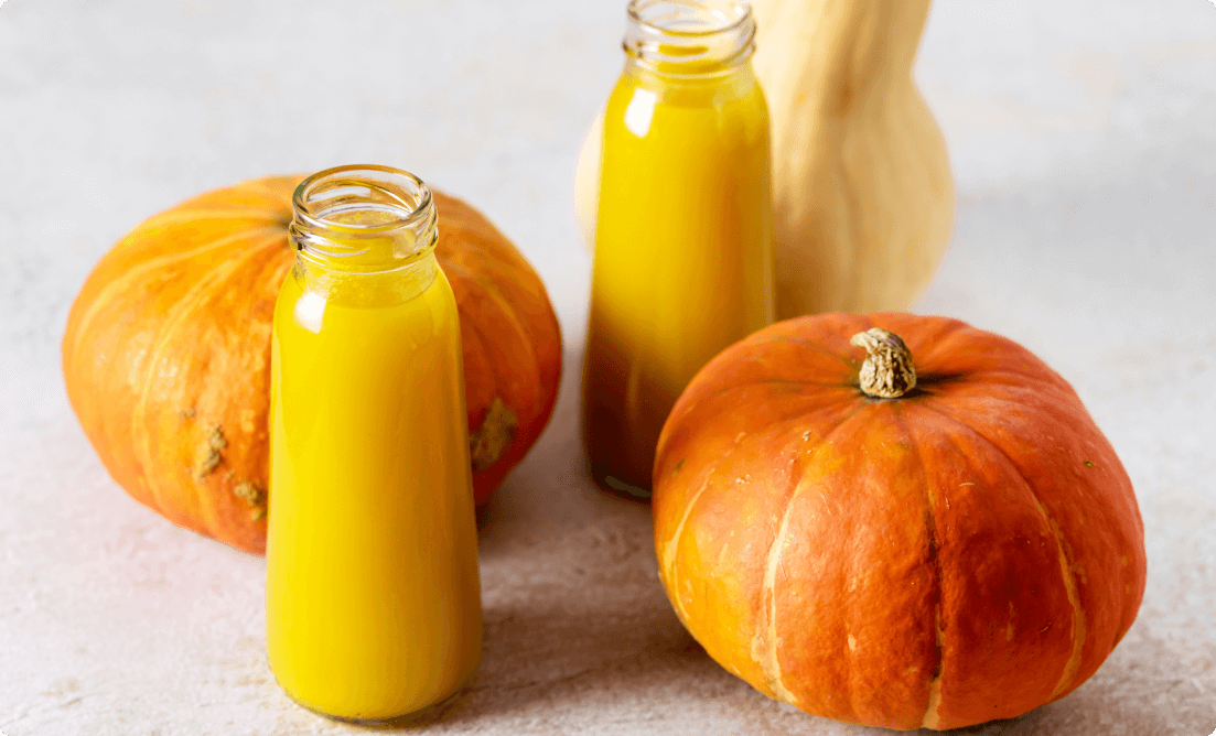 A pair of pumpkins and two bottles full of orange juice are placed on a table. These will keep you fit and healthy throughout the fall season.