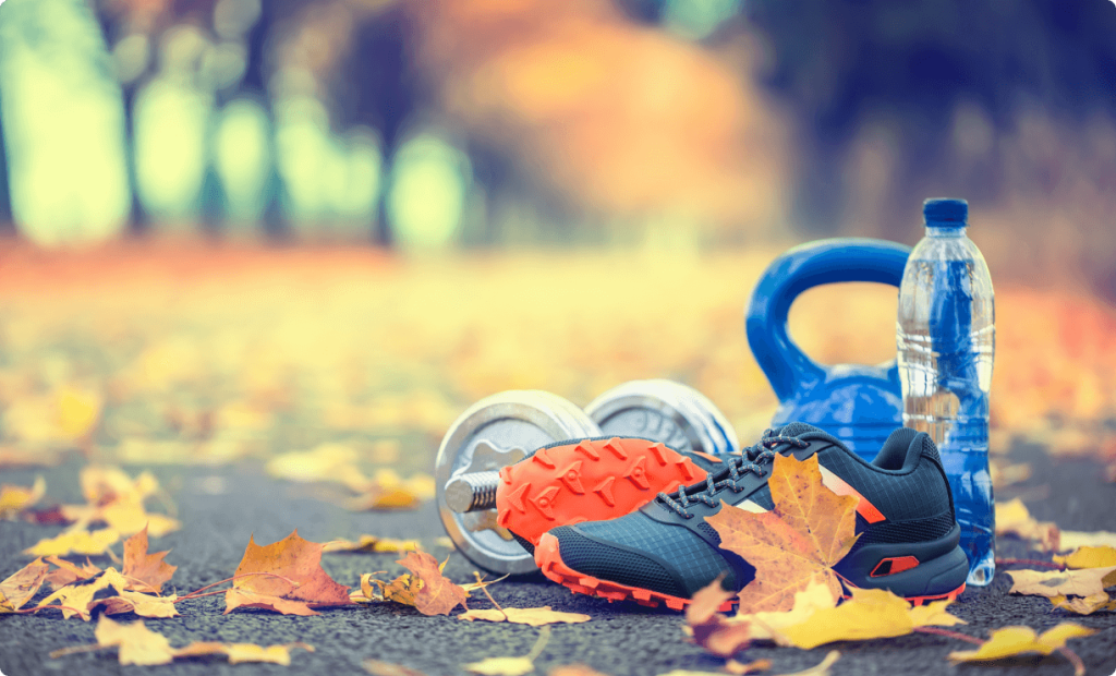 Pair of running shoes water and dumbbells laid on a road with maple leaves - accessories for run exercise or workout activity.