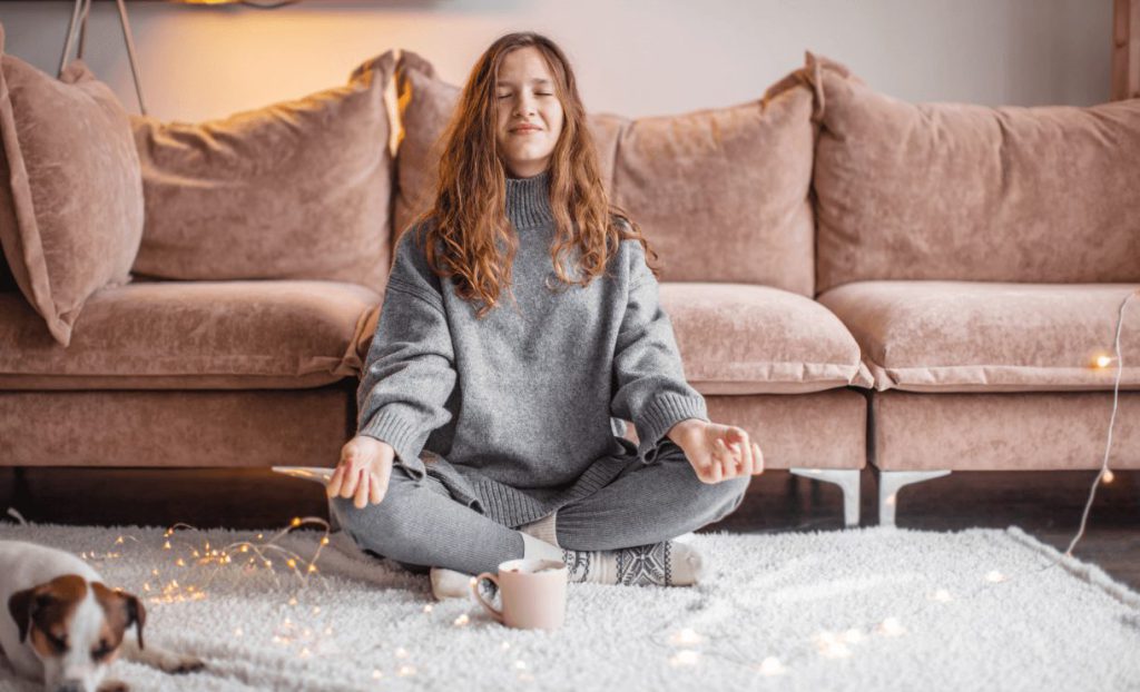 A girl meditating in her lounge wearing cosy winter clothes.