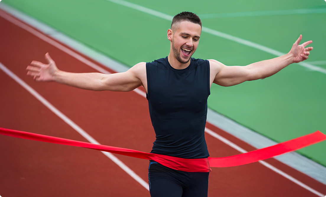 A triumphant male athlete crossing the finish line on a track, celebrating success and peak performance powered by Vision Elite Training.